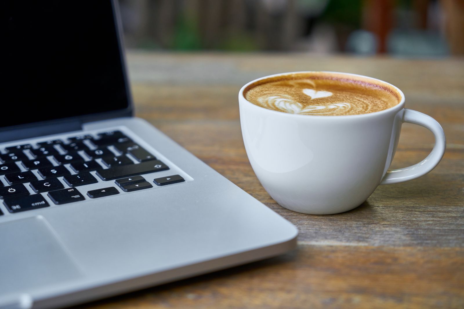 Notebook aberto ao lado de uma xícara de café com leite sobre uma mesa de madeira.